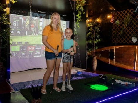 Two people playing indoor virtual golf.
