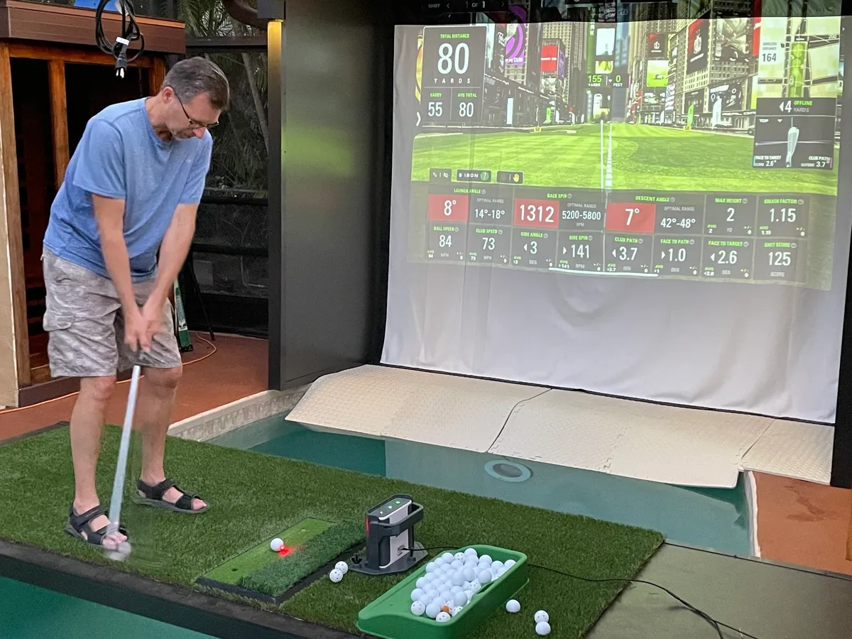Man playing indoor golf with simulator screen.