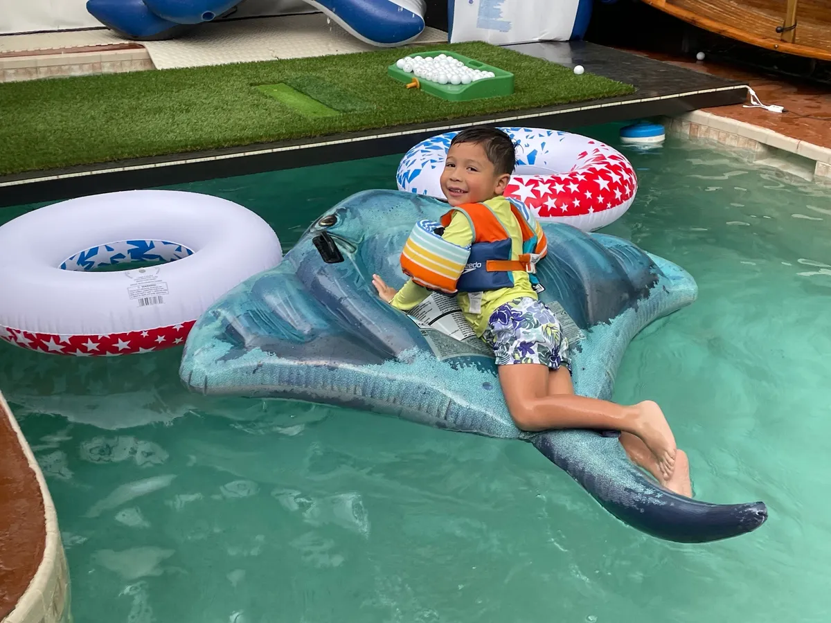 Child on inflatable stingray in pool.