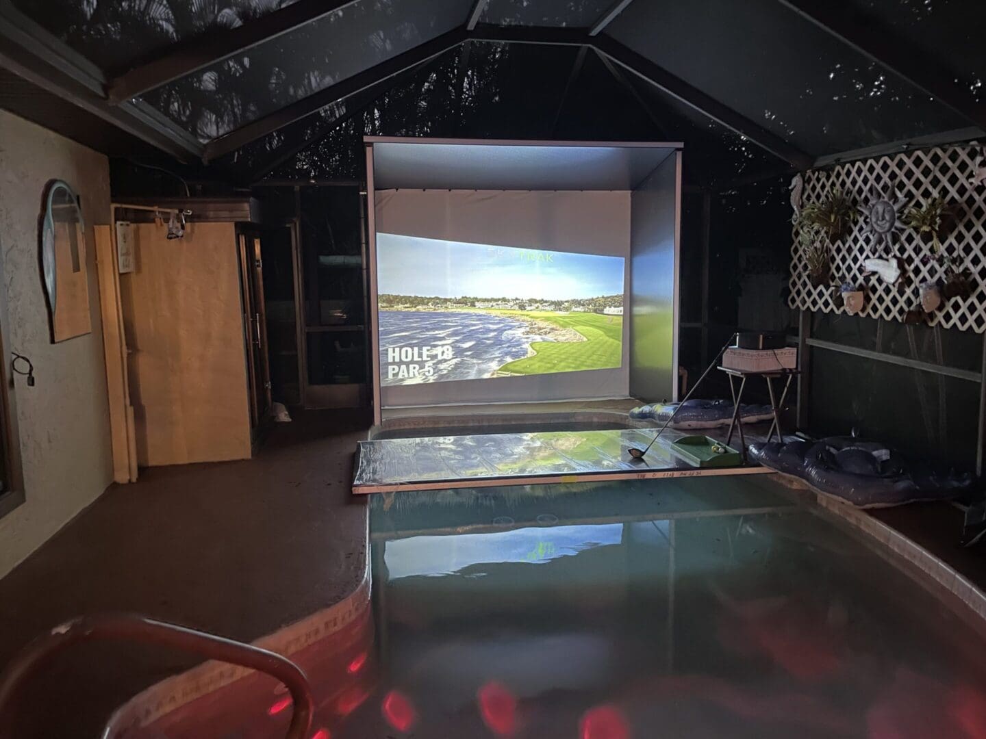 Indoor golf simulator beside swimming pool.