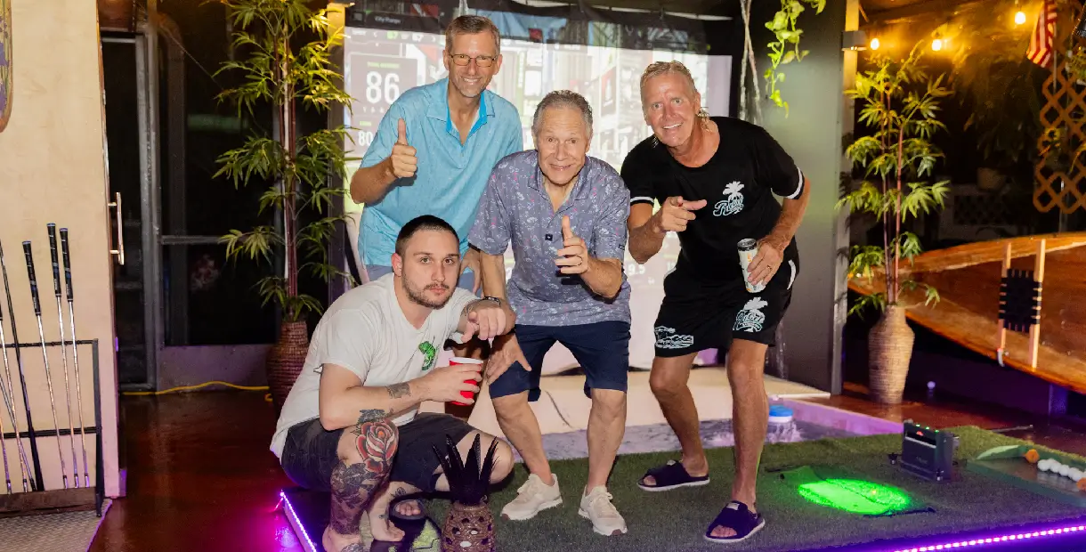 Four men posing with drinks indoors.